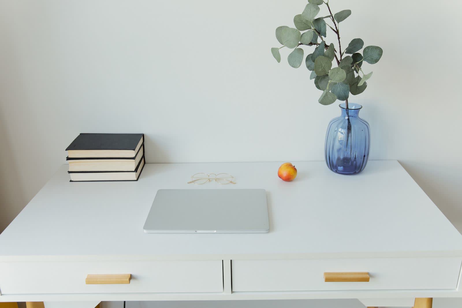 Opgeruimd wit bureau met een gesloten laptop, boeken en een plant