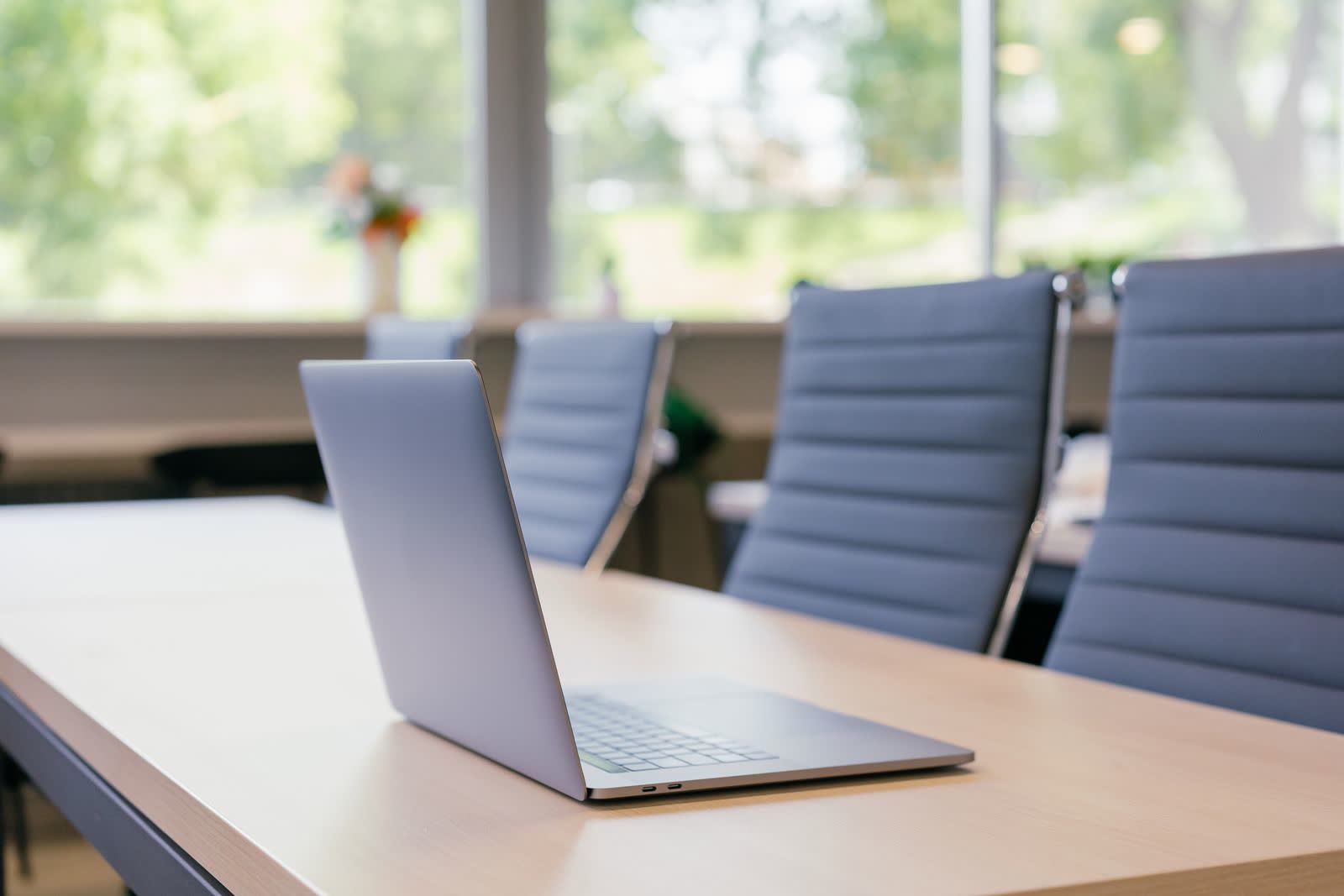 Laptop op een lichte houten vergadertafel in een rustige ruimte met daglicht